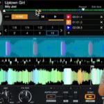 Phil Morse holds up two fingers against a DJ software screen showing Billy Joel's "Uptown Girl" loaded on a deck with a loop active.