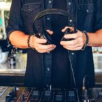 5 DJ Trends To Watch In 2026 (According To 22,000 DJs) Close-up on a DJ holding headphones over gear in a pro DJ booth.