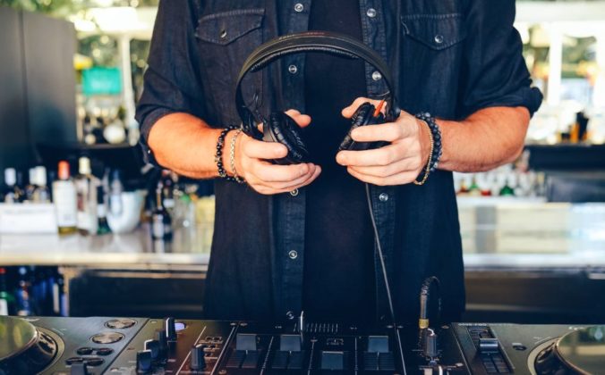 Close-up on a DJ holding headphones over gear in a pro DJ booth.