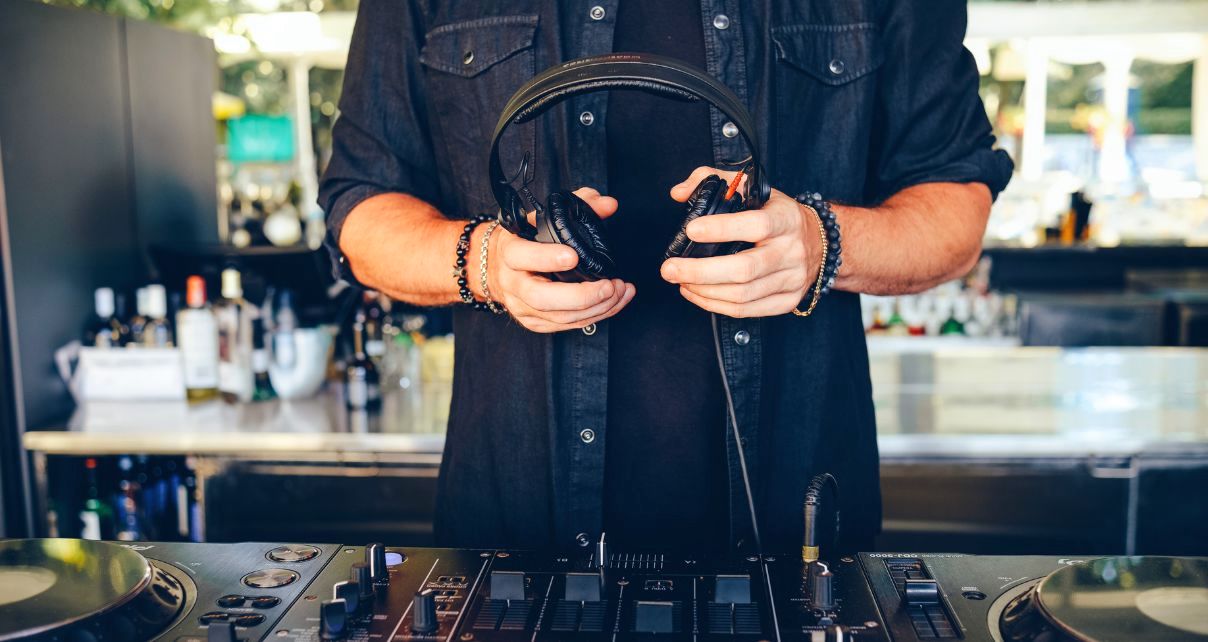 Close-up on a DJ holding headphones over gear in a pro DJ booth.