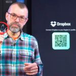 Phil Morse holds up a USB drive with a red X and circle arrow graphic overlaid, standing in front of a Rane System One DJ unit and a screen showing the Dropbox Engine DJ profile connection page with a QR code.