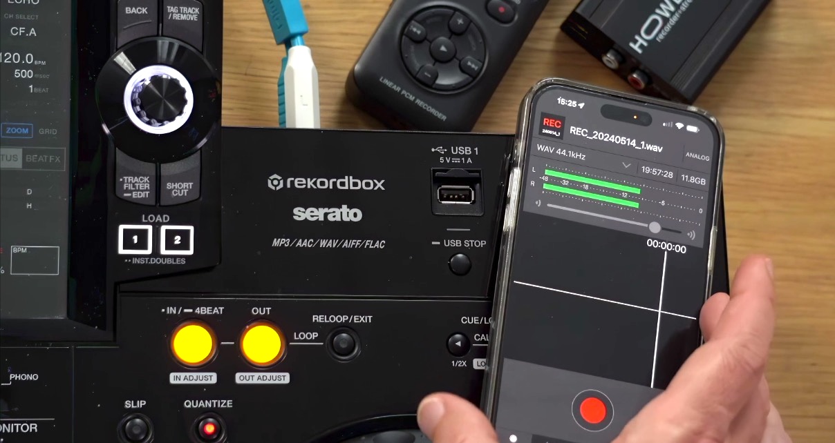 A hand holds a smartphone running the Pioneer DJ REC app above a DJ controller, with other recording devices visible in the background.