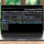 The Rekordbox Trick That Gives You More Hot Cues Per Track A silver laptop sits on a light wooden table displaying Rekordbox DJ software. The room is well lit with lots of windows and greenery in the background.